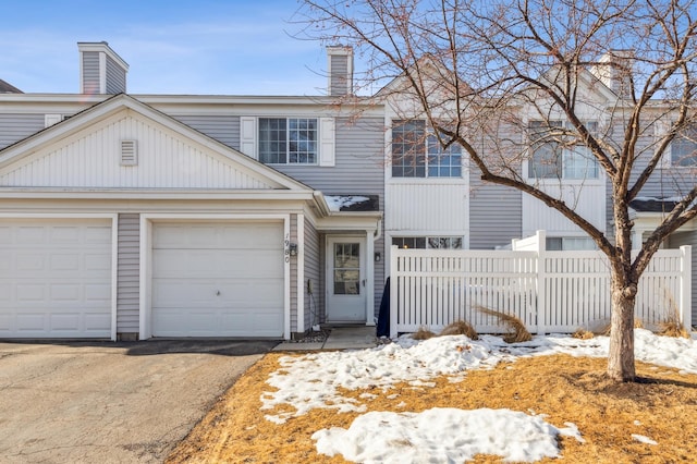 view of front facade featuring aphalt driveway, a chimney, an attached garage, and fence