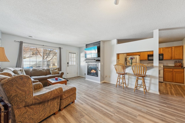 living room featuring a textured ceiling, light wood-style floors, baseboards, and a large fireplace