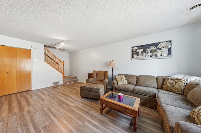 living area with visible vents, a textured ceiling, light wood-style flooring, and stairway