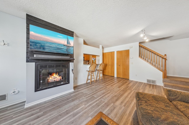 living area with wood finished floors, visible vents, a fireplace, stairs, and a textured ceiling