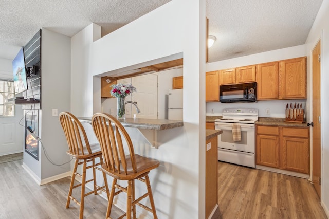 kitchen featuring a kitchen bar, light wood-style flooring, brown cabinets, white appliances, and a textured ceiling