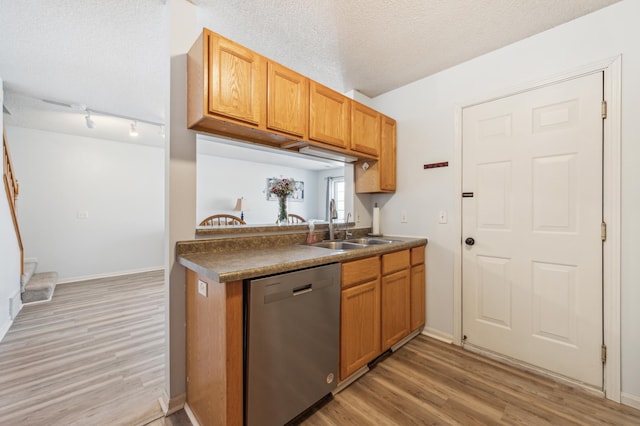 kitchen featuring dark countertops, light wood finished floors, dishwasher, a textured ceiling, and a sink