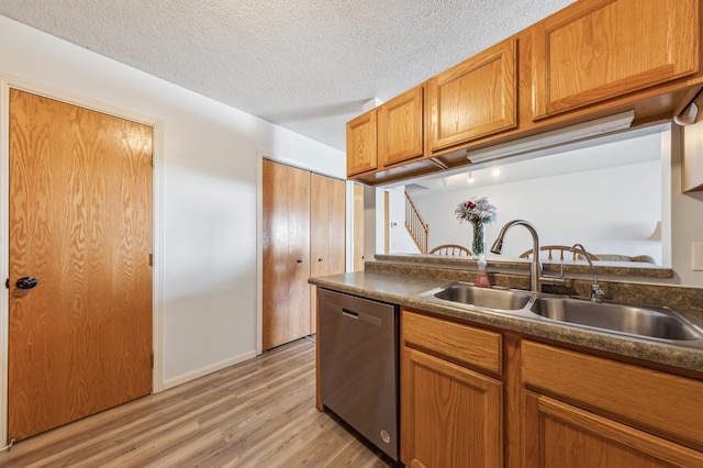 kitchen with dark countertops, light wood finished floors, stainless steel dishwasher, brown cabinetry, and a sink