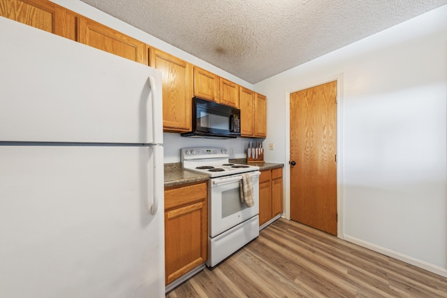 kitchen featuring dark countertops, a textured ceiling, white appliances, light wood-style floors, and brown cabinetry