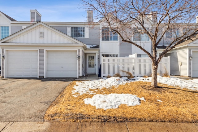 townhome / multi-family property featuring aphalt driveway, a chimney, an attached garage, and fence