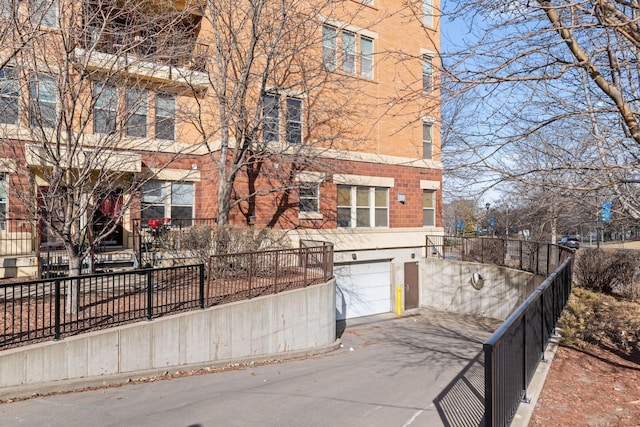 view of side of property featuring an attached garage, fence, brick siding, and driveway