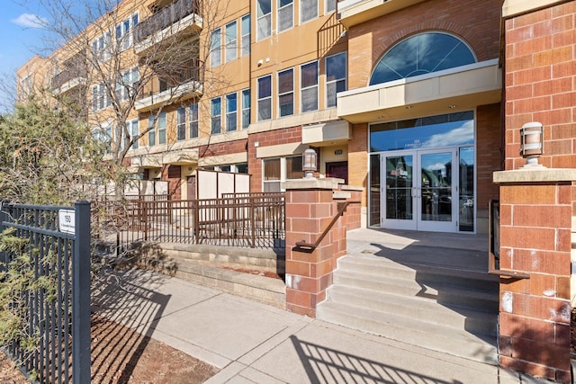 doorway to property featuring brick siding, french doors, and fence