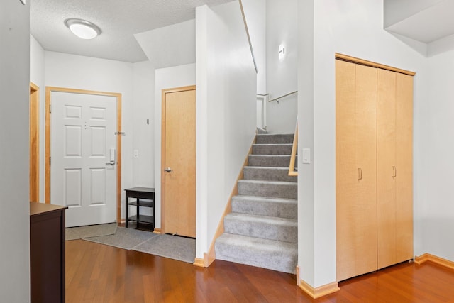 stairs with a textured ceiling, baseboards, and wood finished floors