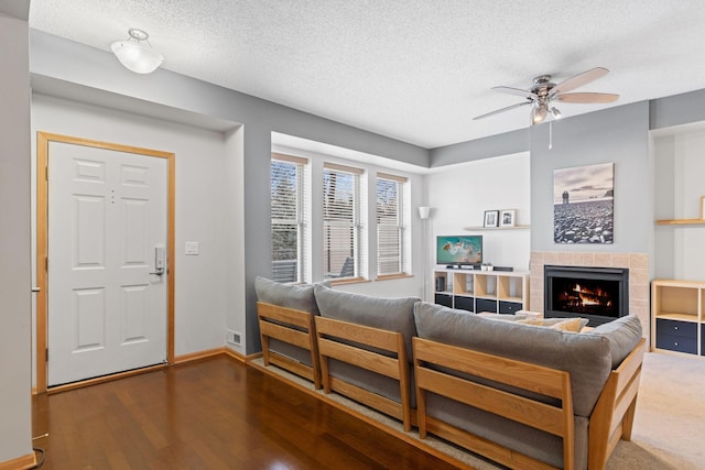 living room with wood finished floors, baseboards, a fireplace, ceiling fan, and a textured ceiling