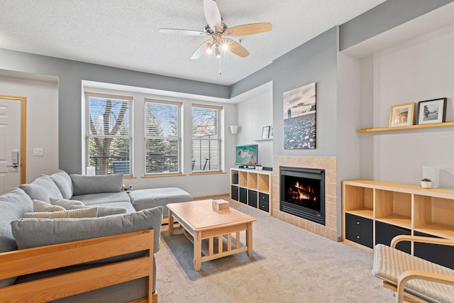 living area with a ceiling fan, a textured ceiling, carpet flooring, and a tile fireplace