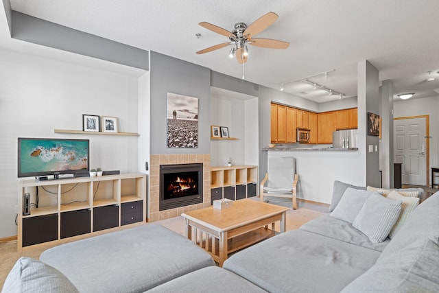 living area featuring light carpet, a textured ceiling, baseboards, ceiling fan, and a tile fireplace