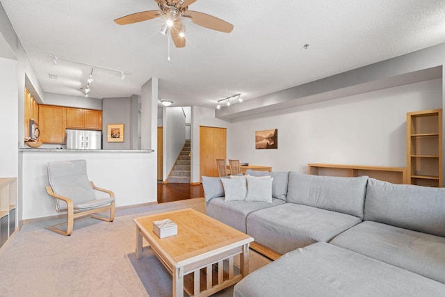 carpeted living area featuring stairs, baseboards, and ceiling fan