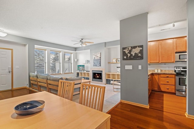 dining room featuring a tiled fireplace, a textured ceiling, baseboards, and wood finished floors