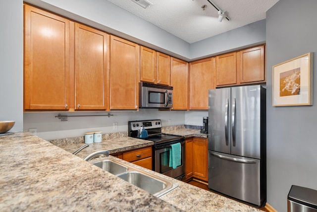 kitchen with a sink, stainless steel appliances, light countertops, rail lighting, and a textured ceiling