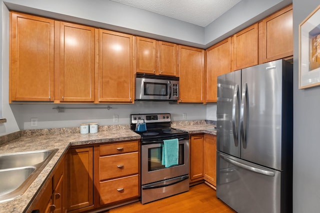 kitchen with light wood-style flooring, a sink, appliances with stainless steel finishes, a textured ceiling, and brown cabinets