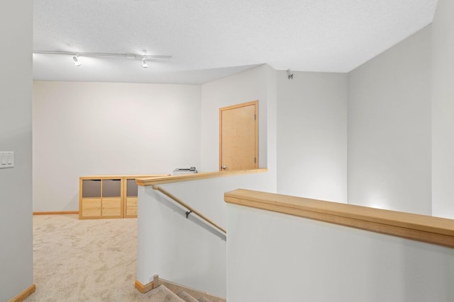 corridor with track lighting, baseboards, light carpet, an upstairs landing, and a textured ceiling