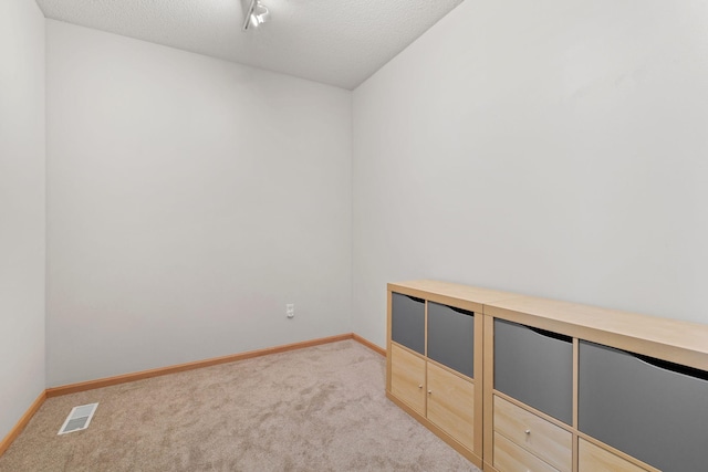 spare room with light carpet, visible vents, and a textured ceiling