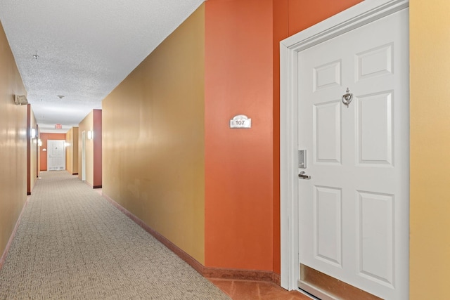 corridor with carpet flooring, a textured ceiling, and baseboards