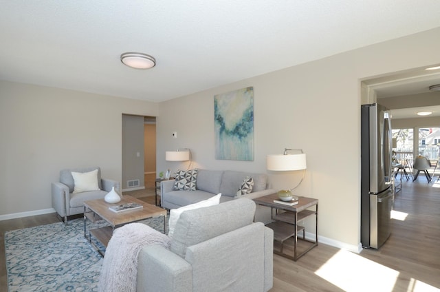 living room with light wood finished floors, visible vents, and baseboards