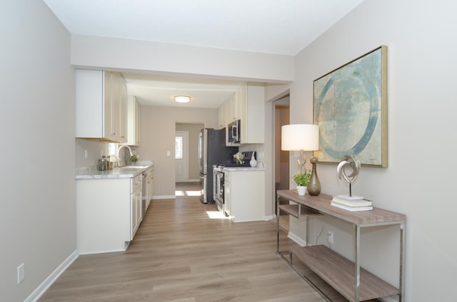 corridor with light wood-style floors, baseboards, and a sink