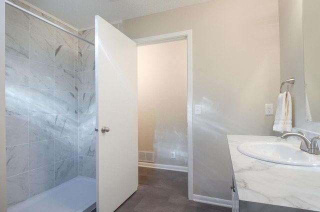 bathroom with tiled shower, visible vents, vanity, and baseboards