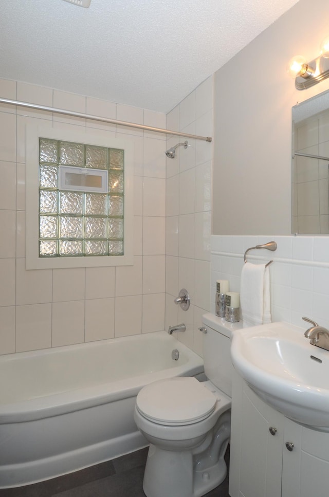 bathroom featuring a wainscoted wall, toilet, a textured ceiling, tile walls, and shower / bathtub combination