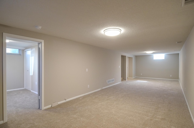 basement featuring light carpet, visible vents, a textured ceiling, and baseboards