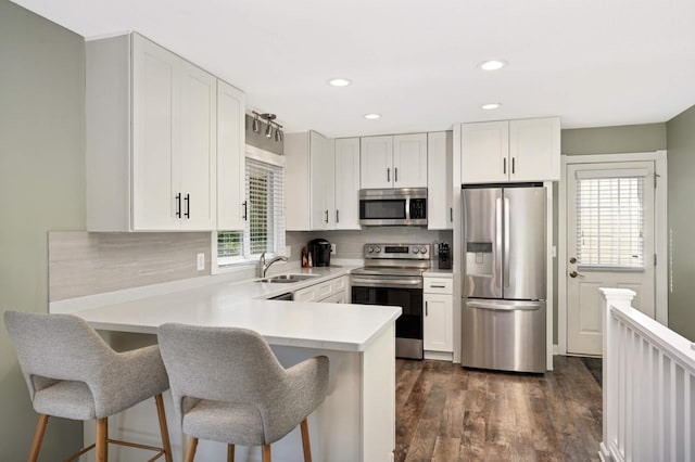 kitchen with tasteful backsplash, white cabinetry, appliances with stainless steel finishes, a peninsula, and light countertops