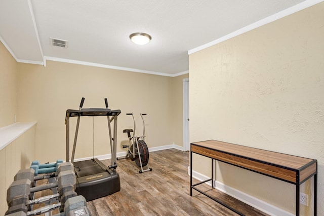 workout area featuring visible vents, ornamental molding, baseboards, and wood finished floors