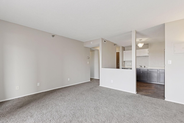 unfurnished living room with baseboards, dark colored carpet, and a sink