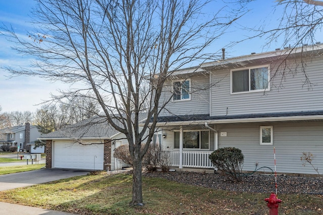 traditional-style house with brick siding, aphalt driveway, a front yard, covered porch, and a garage