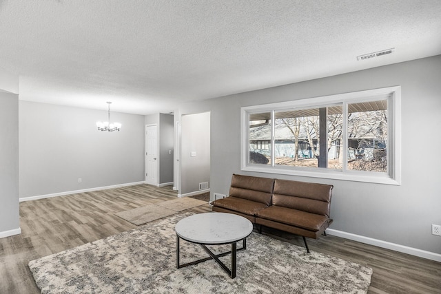 living area with wood finished floors, visible vents, baseboards, a textured ceiling, and a chandelier