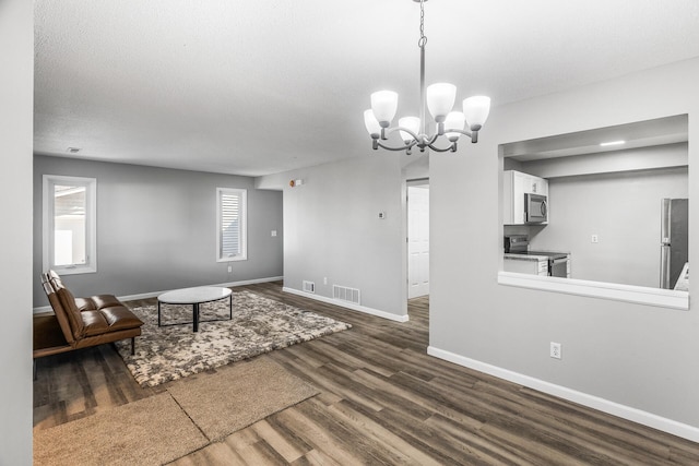 unfurnished living room with dark wood finished floors, baseboards, visible vents, and a chandelier