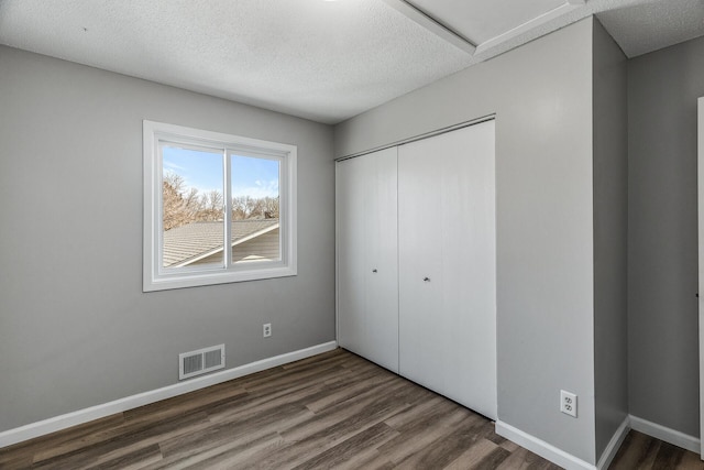 unfurnished bedroom featuring visible vents, baseboards, wood finished floors, a closet, and a textured ceiling