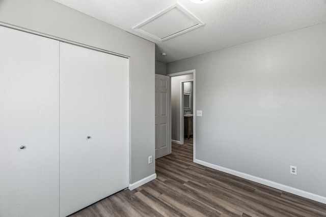 unfurnished bedroom with attic access, baseboards, dark wood-style flooring, and a closet