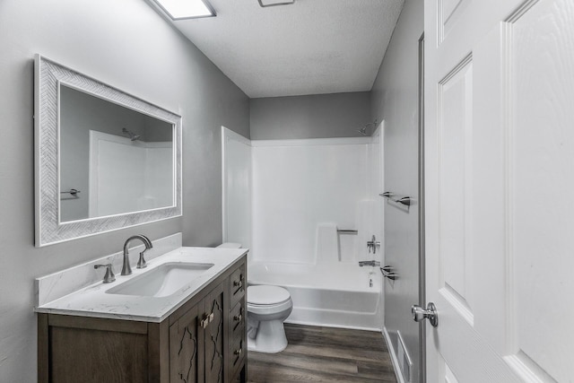 bathroom with toilet, vanity, wood finished floors, a textured ceiling, and  shower combination