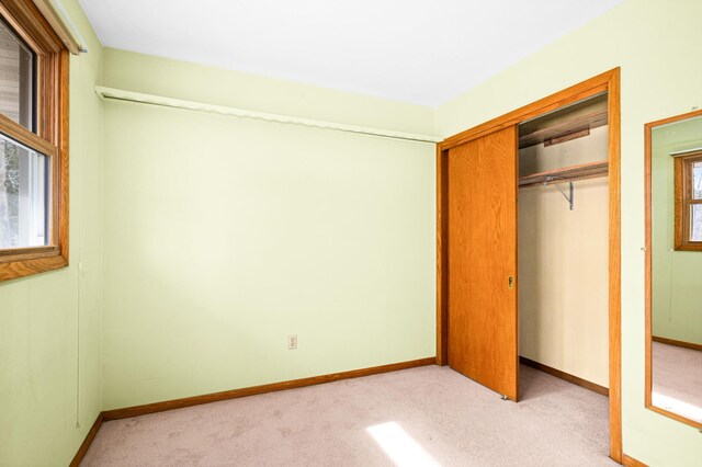 unfurnished bedroom with light carpet, baseboards, and a closet
