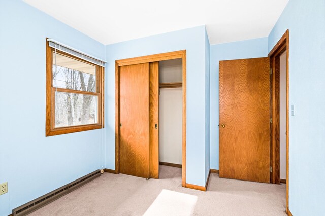 unfurnished bedroom featuring carpet floors, baseboards, a closet, and a baseboard heating unit