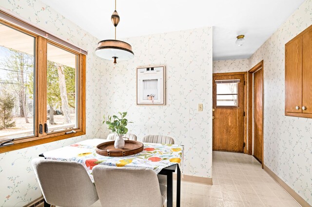 dining room featuring baseboards, wallpapered walls, and light floors