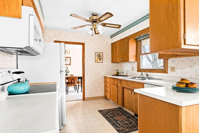 kitchen featuring white appliances, wallpapered walls, a sink, a ceiling fan, and light floors