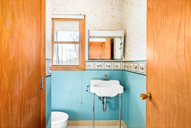 bathroom featuring wallpapered walls, toilet, and a sink