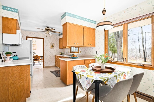 kitchen with light countertops, a peninsula, ceiling fan, wallpapered walls, and light floors