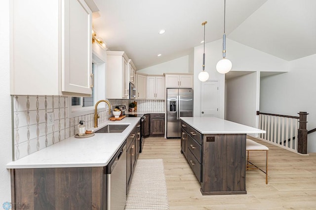 kitchen with a sink, a kitchen breakfast bar, light wood-style floors, appliances with stainless steel finishes, and light countertops