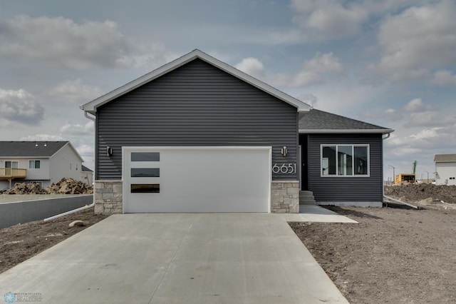 view of front of home featuring a shingled roof, an attached garage, concrete driveway, and stone siding