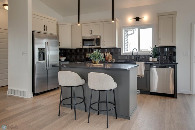 kitchen with a kitchen island, dark countertops, a kitchen bar, light wood-type flooring, and stainless steel appliances