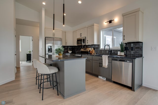 kitchen featuring dark countertops, a kitchen breakfast bar, tasteful backsplash, a sink, and stainless steel appliances