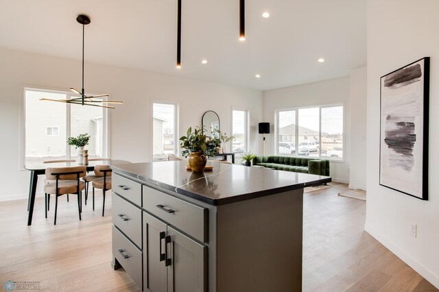 kitchen featuring pendant lighting, a kitchen island, dark countertops, light wood-style floors, and baseboards