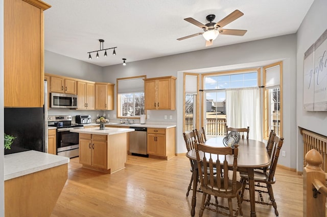 kitchen featuring a ceiling fan, stainless steel appliances, light countertops, light wood-type flooring, and a center island