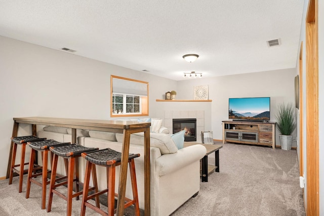 living area featuring a textured ceiling, visible vents, light colored carpet, and a tile fireplace