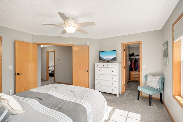 bedroom featuring light carpet, a textured ceiling, a closet, ceiling fan, and a spacious closet